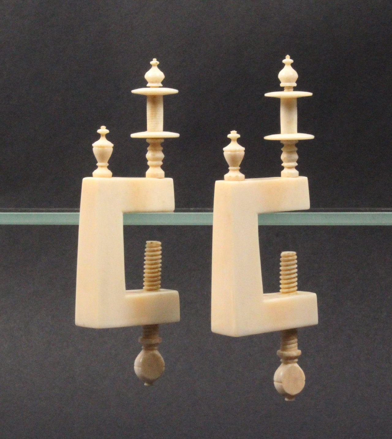 A pair of ivory winding clamps, circa 1820, the rectangular frames with turned urn form finials