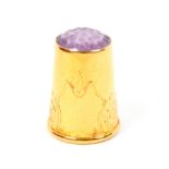 A continental gold thimble, inset polished stone purple top, the plain sides engraved with leaf