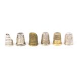 Six thimbles comprising a Georgian silver thimble guard, an English silver thimble with finger