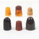 Six thimbles comprising a carved bog oak example, three amber, a vegetable ivory and a serpentine