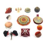 Twelve pin cushions and emeries including two fruit emeries, a pair of cloth hats, a natural walnut,