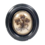 A hair picture in the form of three flowers united by leaves, oval, below a convex glass in ebonised