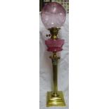 A brass Corinthian column Table Oil Lamp with cranberry glass reservoir and etched shade, on a