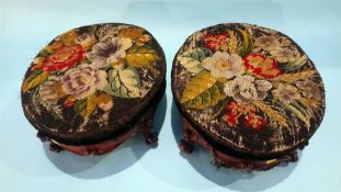 A pair of decorated oval footstools, with embroidered tops, supported on scrolled legs.