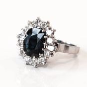 An 18ct white gold sapphire and diamond ring, the oval sapphire approx. 5.00ct, the 12 round cut and