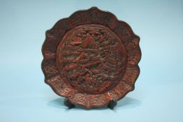A Cinnabar lacquered Chinese plate with shaped rim, the centre decorated with figures and temples,