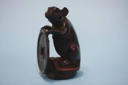 A carved hardwood netsuke in the form of a mouse holding tsuba