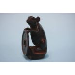 A carved hardwood netsuke in the form of a mouse holding tsuba