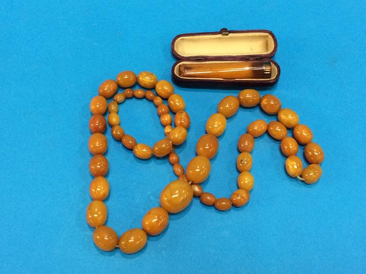 String of amber coloured beads, 61.5 grams and a gold mounted amber coloured cigarette holder