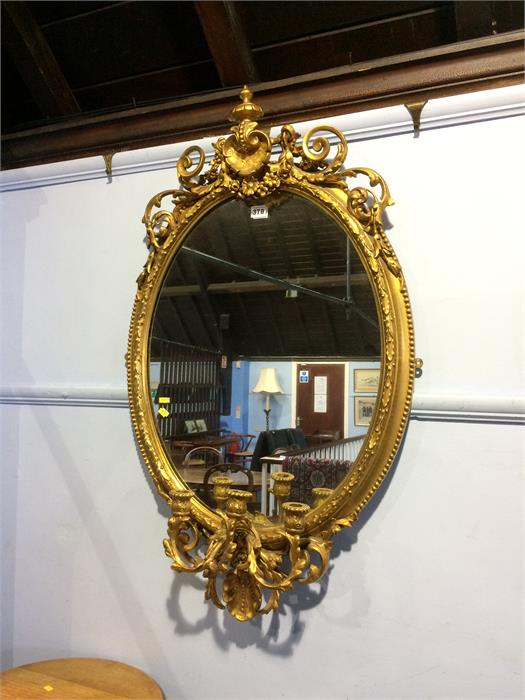 An ornate gilt oval mirror with three branch candelabra