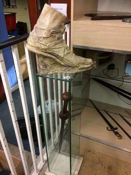 A cast foot resting upon a glass display cabinet containing a sword