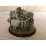 A Lladro figure of two girls and a dog sitting on a settee