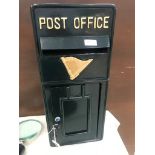 A cast metal post box in dark green with gold motif