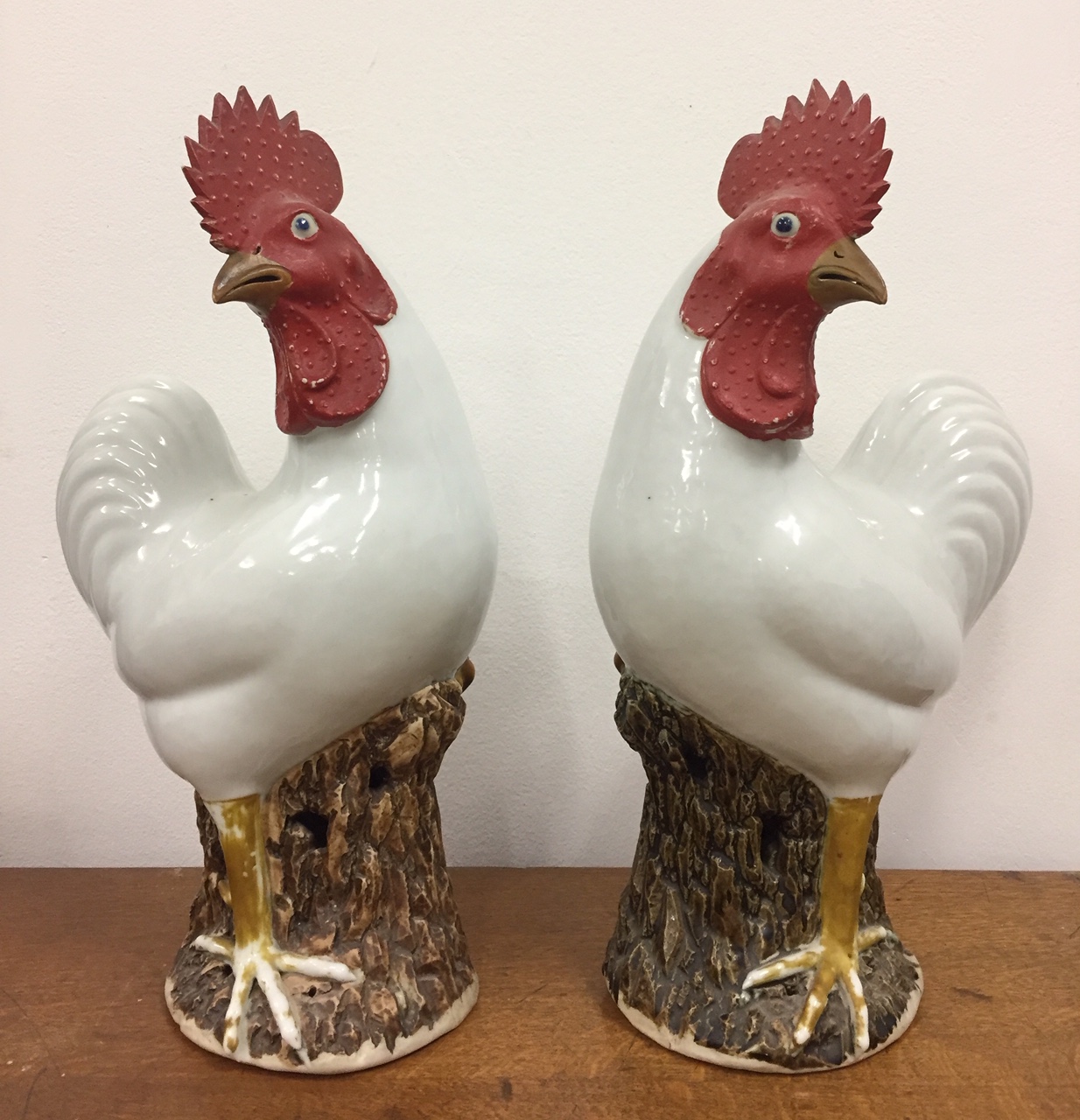 A pair of Chinese Qing Dynasty roosters, on stump bases with glazed white bodies, painted combs,