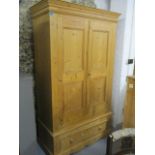 A modern pine wardrobe with a pair of panelled doors, over a long drawer, raised on a bracket