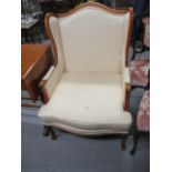 A modern yew finished, wing back armchair, upholstered in a cream fabric, raised on cabriole