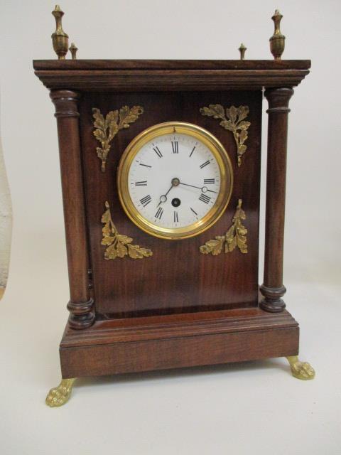 A mahogany cased mantle clock with turned finials, circular dial flanked by oak leaves and four