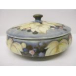 A Moorcroft pottery bowl and cover in the grape and leaf pattern, in tones of brown and red on a