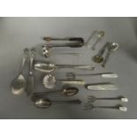 A mixed selection of silver flatware to include two sugar tongs, mother of pearl and silver bladed