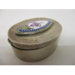 A continental white metal, oval pill box, the hinged lid set with an enamelled panel of a garden urn