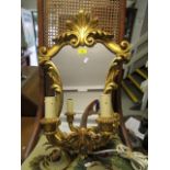 An ornate gilt framed wall mirror with leaf scroll decoration, twin branch candle holders, brass