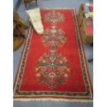 A white painted fibreglass wall plinth with acanthus leaf decoration and a hand woven red ground rug