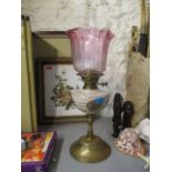 A Victorian oil lamp with a cranberry shade, beige and floral reservoir, on a brass stand
