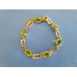 A gold metal coloured bracelet with rectangular links and peridots, in rub-over settings, stamped