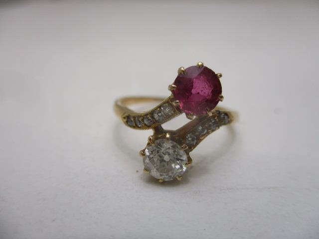A yellow gold coloured metal cross-over ring set with an opposing diamond and ruby, the shoulders