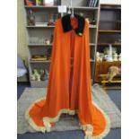 An amateur hand made orange cape with a black faux fur collar and tasselled ends