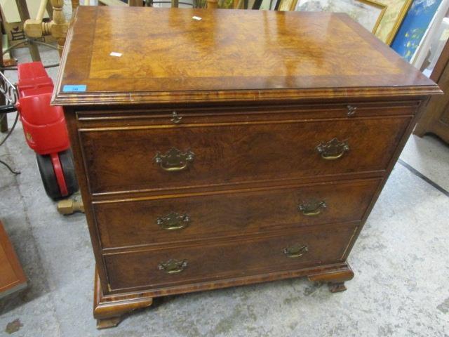 A mid 20th century walnut three drawer chest of drawers having a brushing slide and bracket feet,