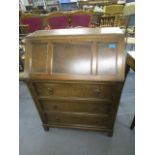 An oak bureau with a fielded fall flap revealing a fitted pigeonhole interior, over three drawers on