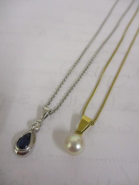 A gold coloured metal necklace with a pearl pendant and a white gold necklace with a sapphire and