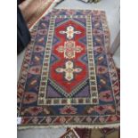 A red ground Turkish rug with three floral, central medallions, flanked by an oatmeal band with rams