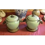 A pair of Celadon green glazed lidded Jars with chamois ram mask handles and bronze circular stands,