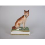 A Derby porcelain seated Fox with painted details on green and gilt base, 4in, A/FFOOTNOTE: A