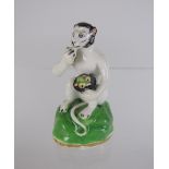 A Rockingham Model of a seated Monkey with bowl of fruit on green painted mound having gilt band,