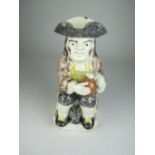 A Whieldon type pottery Toby Jug with seated figure wearing purple sponged coat, holding flagon