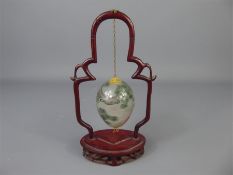 A Vintage Chinese Painted Glass Egg, hanging from a carved rosewood frame.