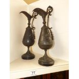 A PAIR OF METAL EWERS (SPELTER?) ON WOODEN BASES WITH A FLORAL REPOUSSE DECORATION