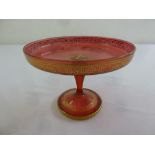 Cranberry glass cake stand on raised circular base with gilt decoration