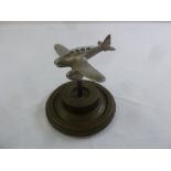 An Art Deco metal paperweight in the form of an aeroplane on turned circular base