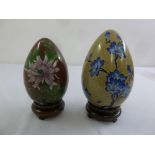 Two cloisonné eggs decorated with flowers and leaves on carved hardwood stands