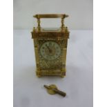 A French brass carriage clock with enamel dial and Arabic numerals, decorative filigree panels and