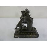 A bronze figurine of a young man carrying a basket reading by a well, mounted on a rectangular