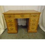 A light oak rectangular kneehole desk with leather top and nine drawers with brass handles