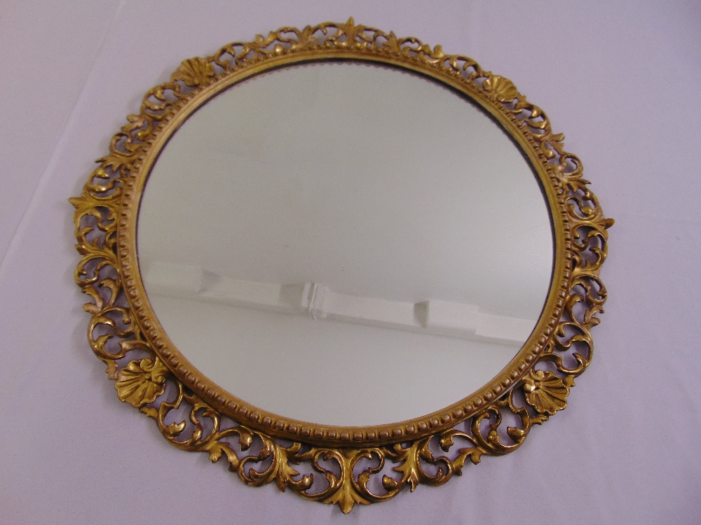 A circular gilded wall mirror with scroll pierced border