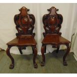 A pair of 19th century mahogany hall chairs, with carved back on scroll legs with paw feet