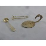 A silver mustard spoon, a pair of silver ice tongs and a white metal cake slice in the form of a