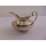 A William IV silver cream jug of compressed circular form with reeded borders, scroll handle on